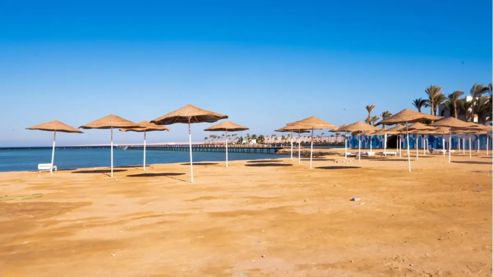 Spiaggia sabbiosa con ombrelloni in paglia e molo al Scandic Beach Resort di Hurghada – Vivere Hurghada