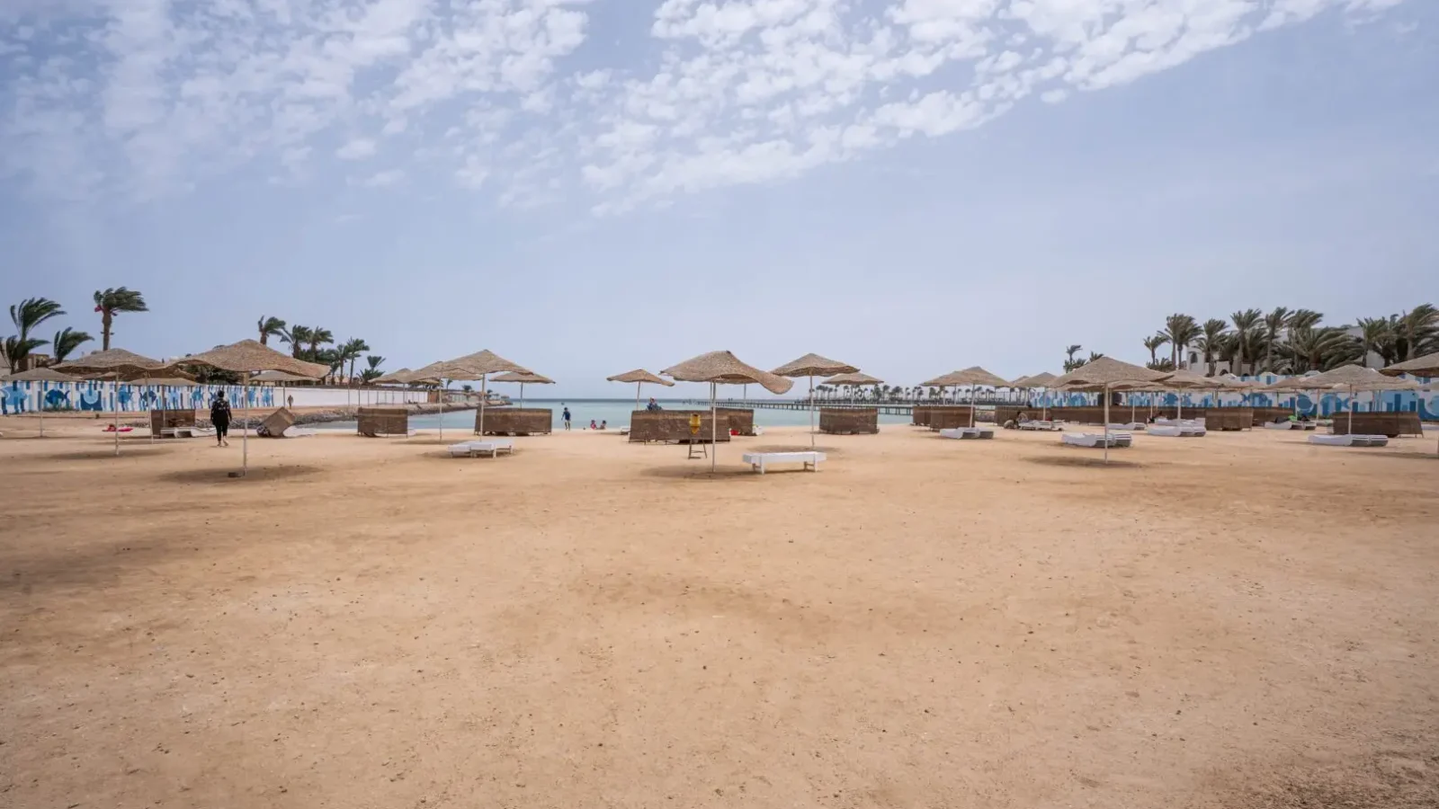 Vista panoramica della piscina con lettini, spiaggia privata sabbiosa attrezzata con ombrelloni, e pontile che si estende sul Mar Rosso dal complesso Scandic Beach Resort a Hurghada, Egitto. Comprare casa a Hurghada, investire a Hurghada, tour immobiliari Hurghada, appartamenti in vendita Hurghada, trasferirsi a Hurghada, vivere in Egitto.